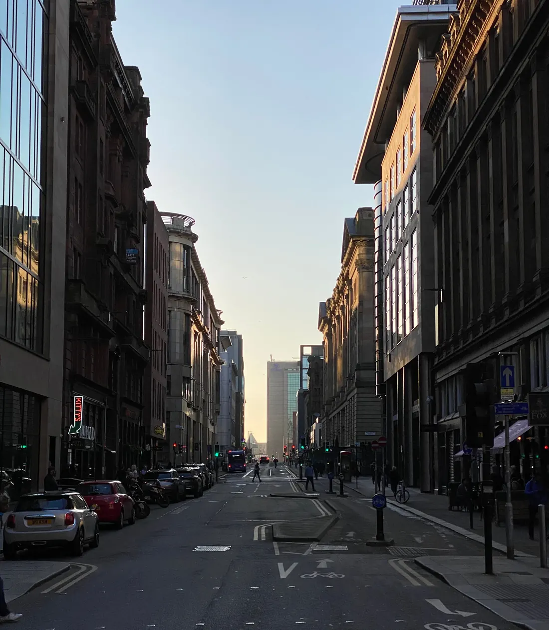 A Glasgow city street at dusk, with local shops and offices along the road.